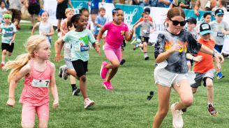 A diverse group of kids running a race through a grass field.