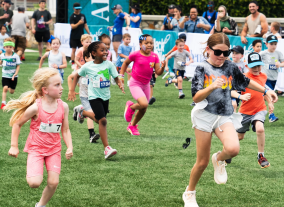 A diverse group of kids running a race through a grass field.